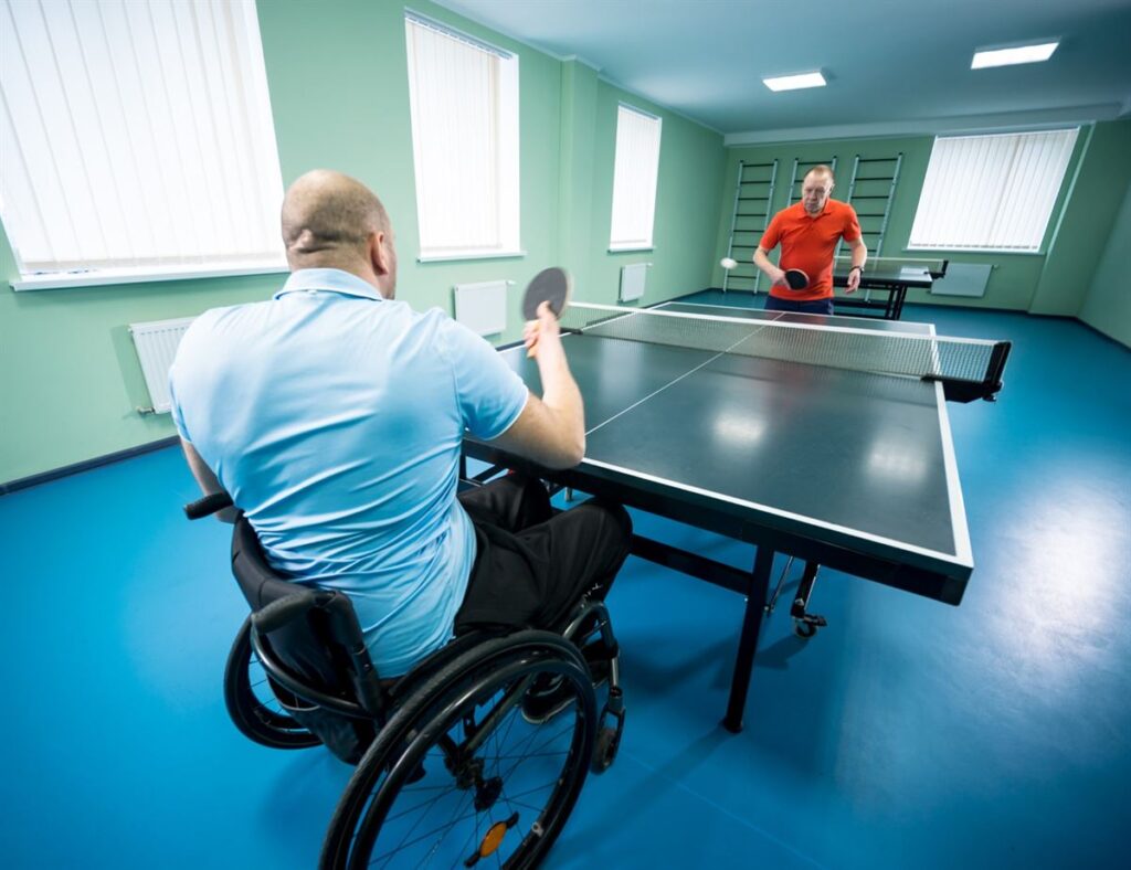 A wheelchair user playing table tennis against a standing opponent