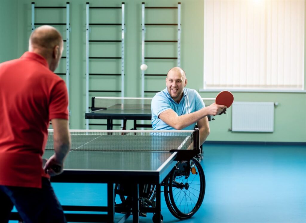 A smiling wheelchair table tennis player returning the ball during a rally