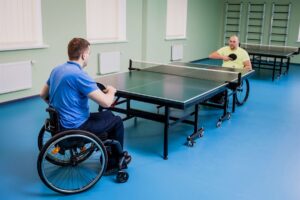 Two wheelchair users playing table tennis against each other indoors
